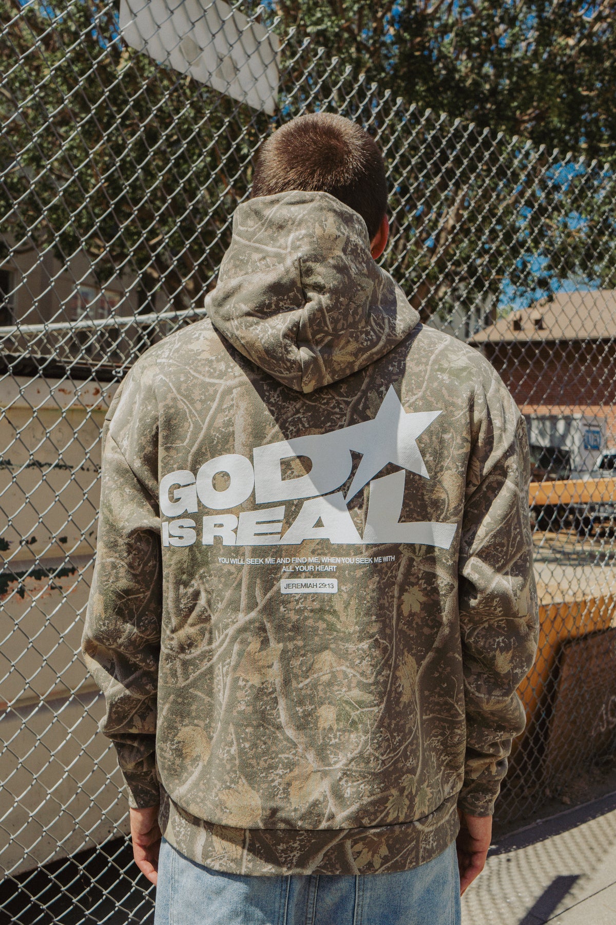 Back view of model in camo God Is Real hoodie with star graphic