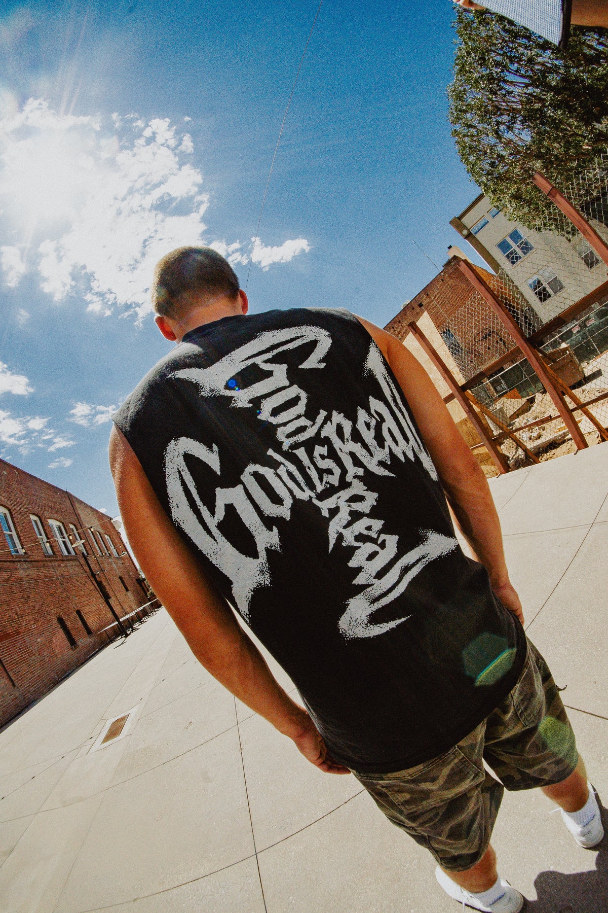Fisheye back view of model in black God Is Real cut-off tank with cross graphic