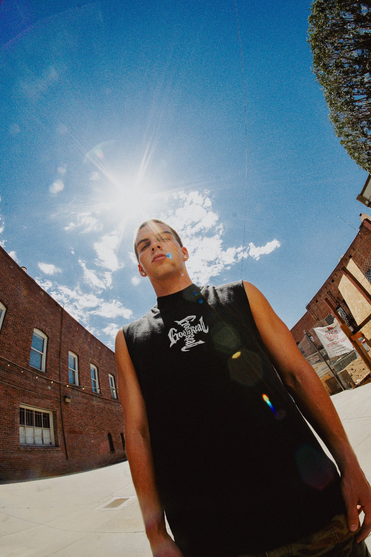 Model wearing black God Is Real cut-off tank under a bright blue sky